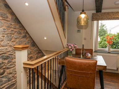 A small dining area with two brown leather chairs a wooden table with flowers and a bottle of wine near a window and staircase at Style Cottage in Keswick
