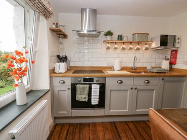 A kitchen with grey cabinets wooden countertop oven stovetop microwave and a window with orange flowers at Style Cottage in Keswick