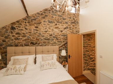 A bedroom with a double bed with beige headboard stone wall and an open wooden door at Style Cottage in Keswick