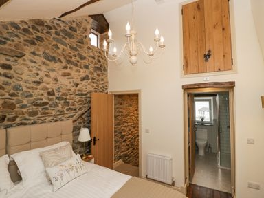 A bedroom with a stone wall a bed with pillows a chandelier and a door leading to a bathroom at Style Cottage in Keswick