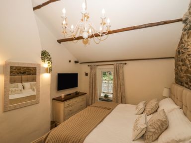 A bedroom with a bed a chest of drawers a window with curtains a mirror and a chandelier at Style Cottage in Keswick