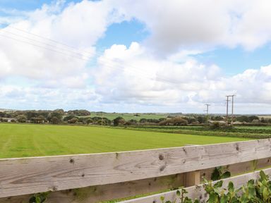 A wooden fence overlooking a green field with trees and power lines under a cloudy sky at Atlantic Reach in Marazion