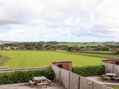 A backyard with wooden picnic tables on a deck and green fields beyond at Atlantic Reach in Marazion