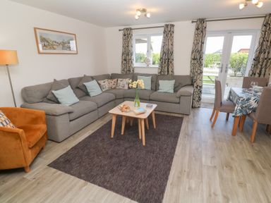 A living room with a gray sectional sofa brown armchair coffee table and dining table at Atlantic Reach in Marazion