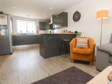 A kitchen with dark cabinets a window with plants a mustard armchair a floor lamp and a gray sofa at Atlantic Reach in Marazion