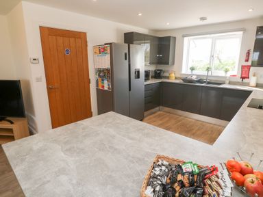 A kitchen with grey cabinets a silver refrigerator a wooden door and a countertop with a basket of snacks at Atlantic Reach in Marazion