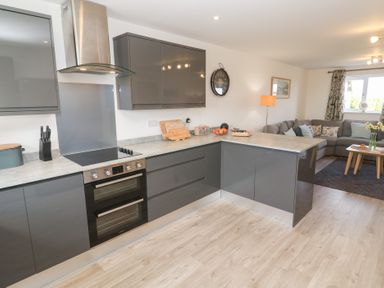 A kitchen with grey cabinets, an oven, stove, and a living area with a grey sofa and coffee table at Atlantic Reach in Marazion