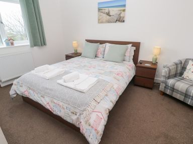 A bedroom with a double bed bedside tables lamps a window with green curtains and a checked armchair at Atlantic Reach in Marazion