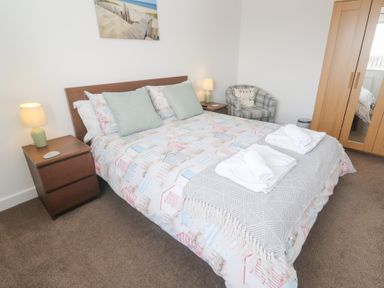 A bedroom with a double bed two bedside tables with lamps a checked armchair and a wooden wardrobe with mirrored doors at Atlantic Reach in Marazion