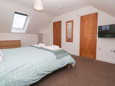 A bedroom with a bed and folded towels on it a wooden door a wall mirror a chest of drawers a skylight window and a mounted television at Atlantic Reach in Marazion