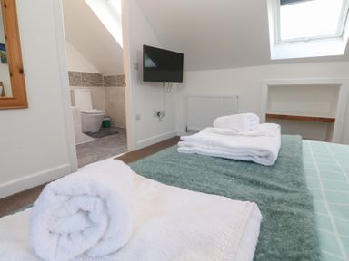 A bedroom with a skylight window and a mounted television with towels on the bed at Atlantic Reach in Marazion