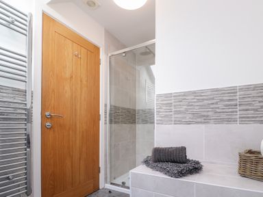 A bathroom with a wooden door a glass shower enclosure a heated towel rail and towels on a tiled surface at Atlantic Reach in Marazion