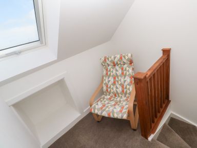 A patterned cushioned chair next to a wooden stair railing under a large window at Atlantic Reach in Marazion