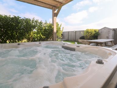 An outdoor hot tub with bubbling water under a wooden pergola next to a picnic table and garden shed at Atlantic Reach in Marazion