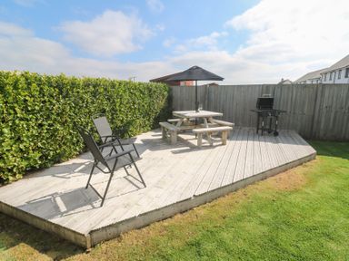 Wooden deck with two black chairs a picnic table with umbrella and a barbecue grill in a fenced garden at Atlantic Reach in Marazion