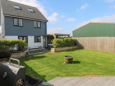 A backyard with green grass a wooden planter with flowers a picnic table a barbecue grill and a two story house at Atlantic Reach in Marazion