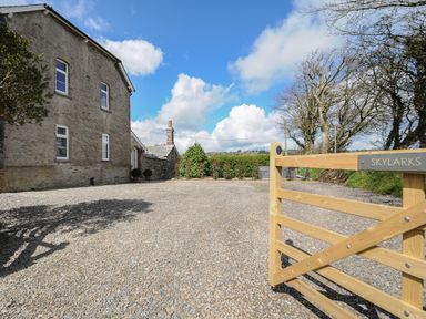 Gravel driveway with wooden gate and stone house under blue sky at Skylarks in No Mans Land near Looe