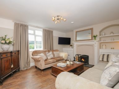 A living room with beige sofas a wooden coffee table a fireplace and a TV on the wall at Skylarks in No Mans Land near Looe