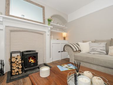 A living room with a fireplace logs throw on a couch and candles on a wooden table at Skylarks in No Man's Land near Looe