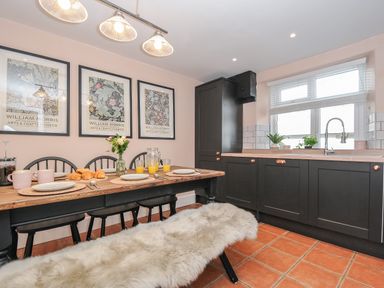 A kitchen with a wooden dining table set with plates croissants and orange juice next to black cabinets and a window with white blinds at Skylarks No Mans Land near Looe