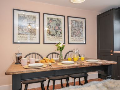 A dining area with a wooden table set for breakfast with plates croissants and juice and three framed William Morris prints on the wall at Skylarks in No Man's Land near Looe