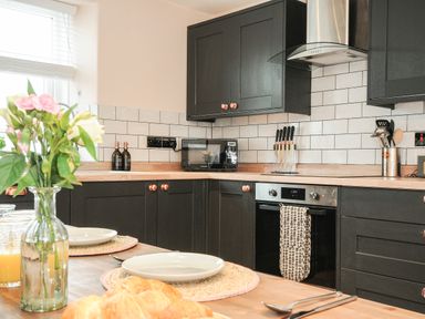 A kitchen with black cabinets a wooden countertop a microwave an oven a knife set and a dining table with plates and flowers at Skylarks in No Man's Land near Looe