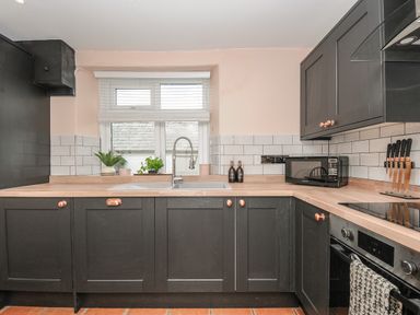 A kitchen with black cabinets wooden countertops a sink a window with blinds a microwave and a knife set at Skylarks in No Man's Land near Looe