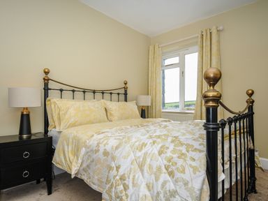 A bedroom with a black metal bed frame with brass details yellow floral bedding matching curtains two black bedside tables with lamps at Skylarks in No Man's Land near Looe
