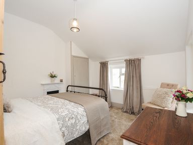 A bedroom with a bed a chair with cushion a table with flowers and a window with curtains at Skylarks in No Mans Land near Looe