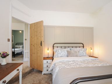 A bedroom with a bed bedside tables lamps and a wooden door leading to another room at Skylarks in No Mans Land near Looe