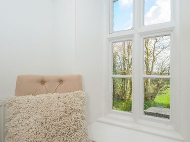 A beige chair with a textured cushion near a white framed window showing trees outside at Skylarks in No Mans Land near Looe