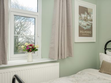 A bedroom corner with a window a vase of flowers beige curtains and a framed Polperro Cornwall poster at Skylarks No Mans Land near Looe