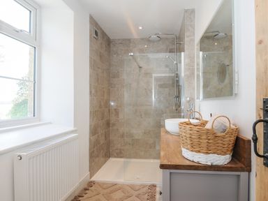 A bathroom with a walk-in shower a wooden countertop with a white vessel sink and a wicker basket at Skylarks in No Man's Land near Looe