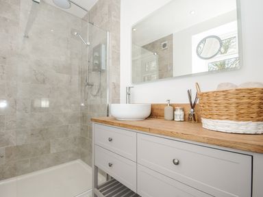 A bathroom with a walk in shower and a wooden countertop with a sink and toiletries at Skylarks in No Man's Land near Looe