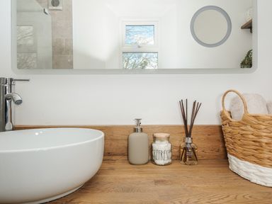 A bathroom countertop with a round white sink soap dispenser glass jar reed diffuser and basket with towels at Skylarks in No Mans Land near Looe