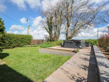 A garden with a hot tub on a paved area surrounded by grass and trees at Skylarks in No Man's Land near Looe