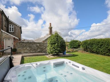 An outdoor area with a hot tub a lawn a stone wall and a building with a door at Skylarks in No Mans Land near Looe