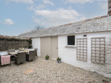 A courtyard with a dining table and chairs on gravel next to white brick walls and a stone wall at Skylarks in No Man's Land near Looe