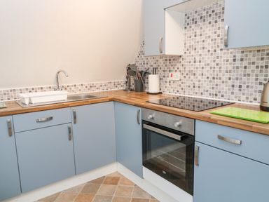 A kitchen with blue cabinets wooden countertops electric stove oven and tiled backsplash at No 51 Valley Lodges in Honicombe Manor near Gunnislake