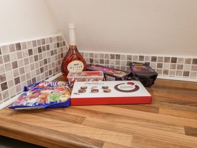 A wooden kitchen countertop with a bottle of Mateus Rose wine and various packaged sweets and chocolates at No 51 Valley Lodges Honicombe Manor near Gunnislake