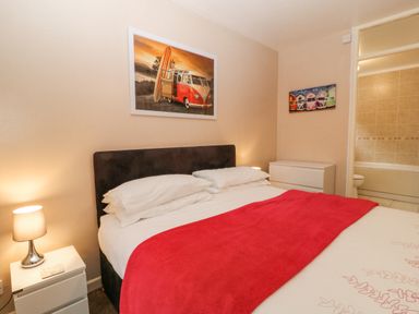 A bedroom with a bed, bedside table with lamp, dresser, and doorway to a bathroom at No 51 Valley Lodges Honicombe Manor near Gunnislake