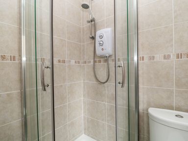 A bathroom shower with glass doors and beige tiled walls next to a white toilet at No 51 Valley Lodges in Honicombe Manor near Gunnislake