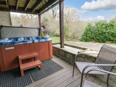 A covered patio with a hot tub wooden steps and a chair overlooking a garden at No 51 Valley Lodges Honicombe Manor near Gunnislake