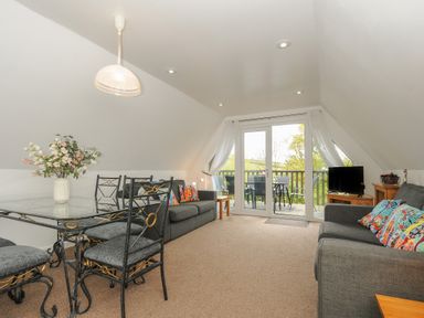 A living room with a glass dining table and chairs two grey sofas with colorful cushions and glass doors leading to a balcony at No 51 Valley Lodges Honicombe Manor near Gunnislake