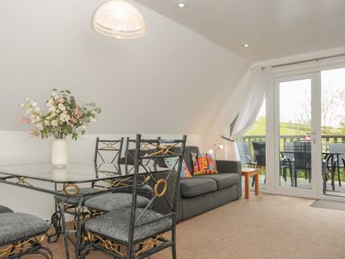A dining area with glass table and metal chairs next to a sofa with colorful cushions and a balcony door at No 51 Valley Lodges Honicombe Manor near Gunnislake