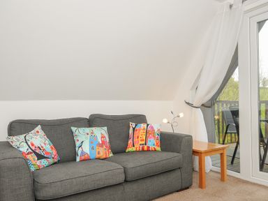 A living room with a gray sofa and colorful cushions next to a wooden side table and glass doors at No 51 Valley Lodges Honicombe Manor near Gunnislake