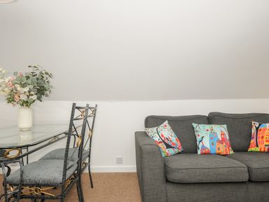 A dining table with chairs and a vase of flowers next to a grey sofa with colorful cushions at No 51 Valley Lodges in Honicombe Manor near Gunnislake