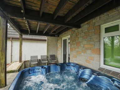 An outdoor covered patio area with a blue hot tub and three metal chairs at No 51 Valley Lodges Honicombe Manor near Gunnislake