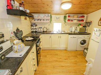 A kitchen with cream cabinets black countertops a stove toaster kettle microwave washing machine dishwasher and refrigerator at Cartron Cottage in Ballintubber County Mayo