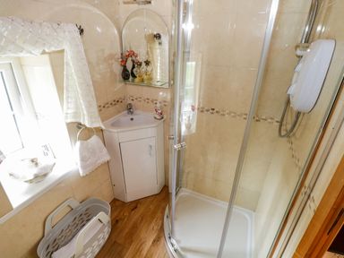 A bathroom with a corner sink cabinet a glass enclosed shower and a window with a towel at Cartron Cottage in Ballintubber County Mayo